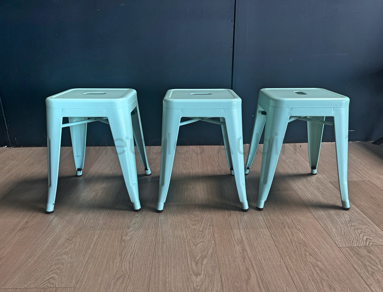 3 petits tabourets devant un mur noir sur un parquet bois clair